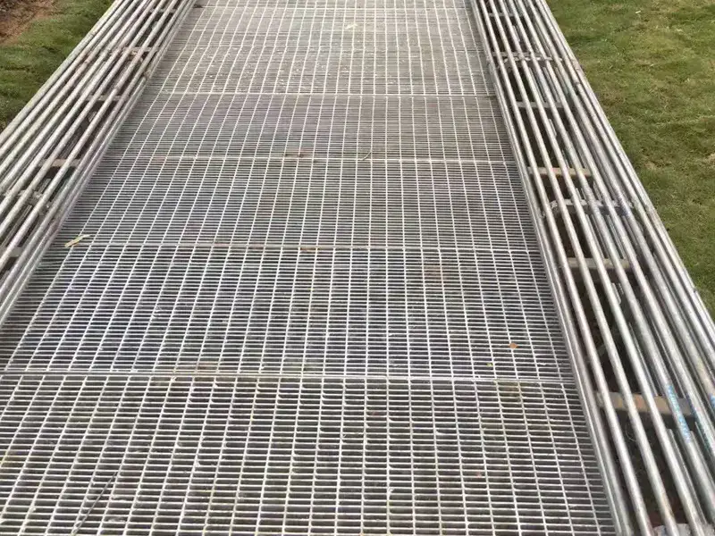 View looking down through galvanized welded grating boardwalk deck over harbor water; visible weld points