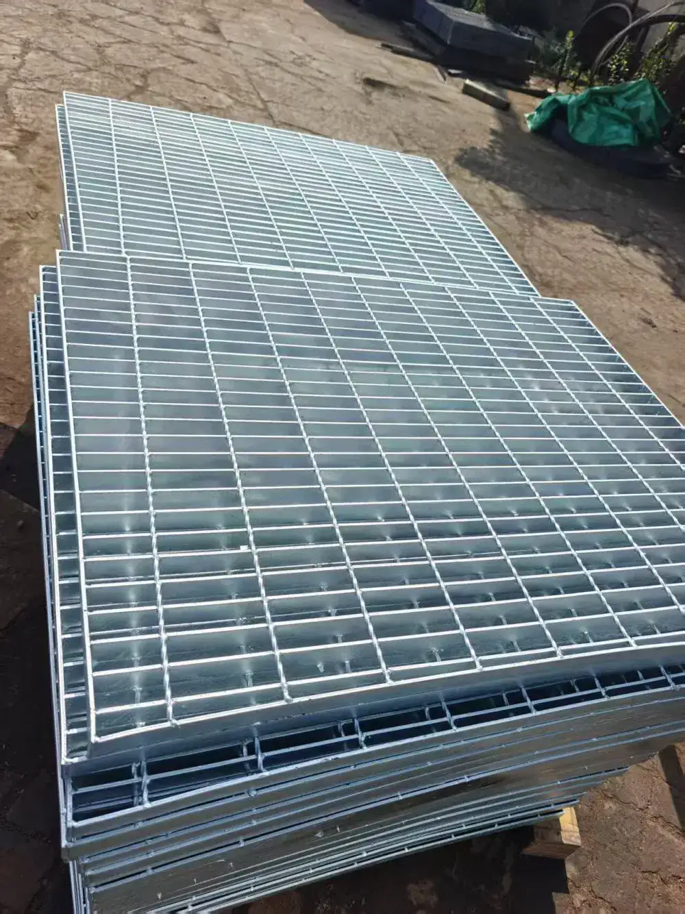 Welded grating walkway panels installed flush between grey paving slabs on outdoor bridge/boardwalk; bordered by metal railings