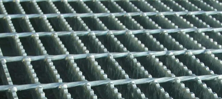 Galvanized welded grating panels stacked upright against warehouse wall in rows