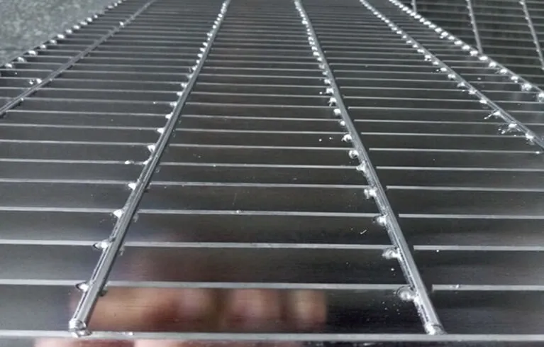 Extreme close-up along length of bright steel grating panels in stockyard; strong surface reflections